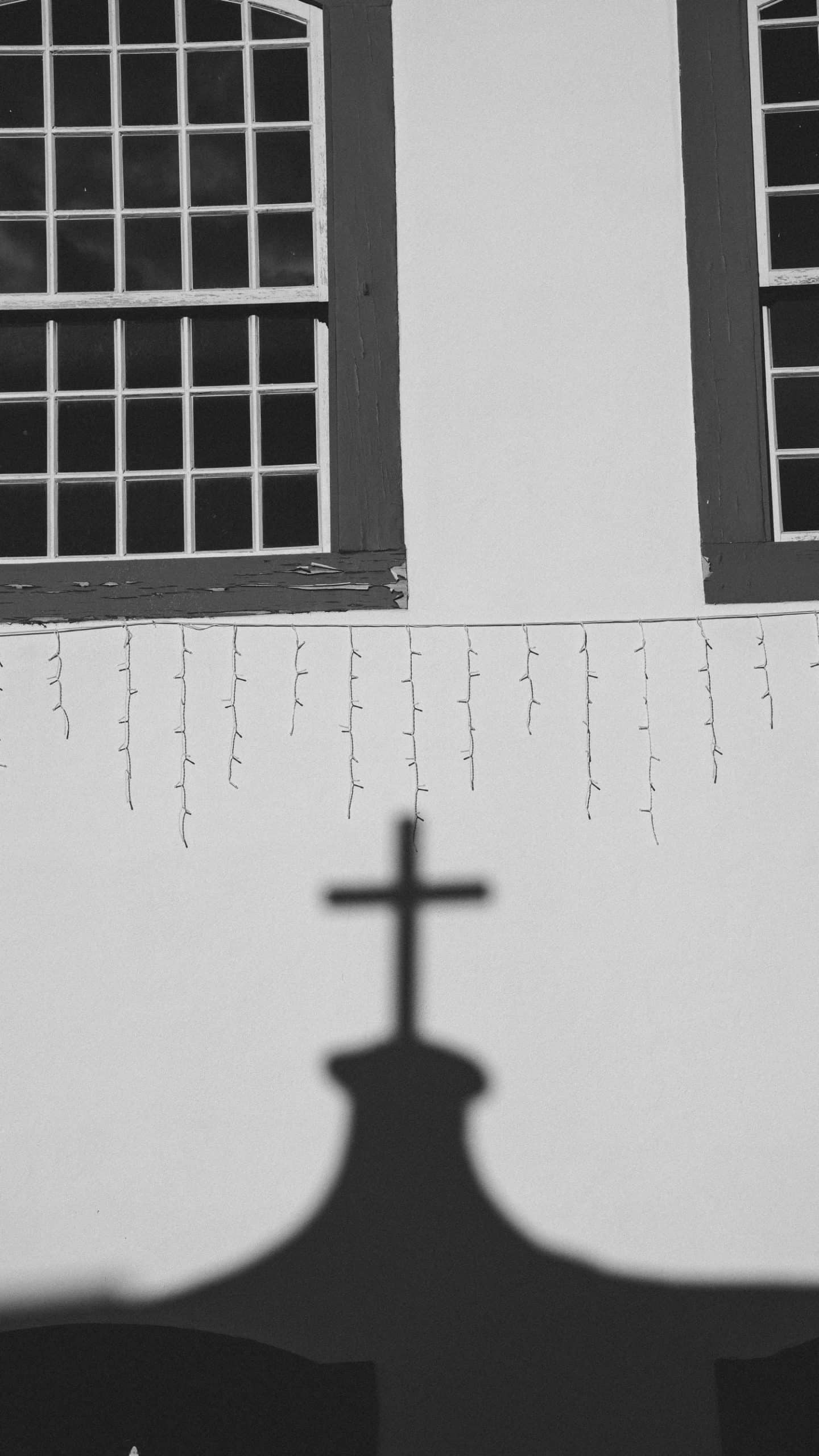 A black and white photo showing a cross shadow on a church wall with two windows.