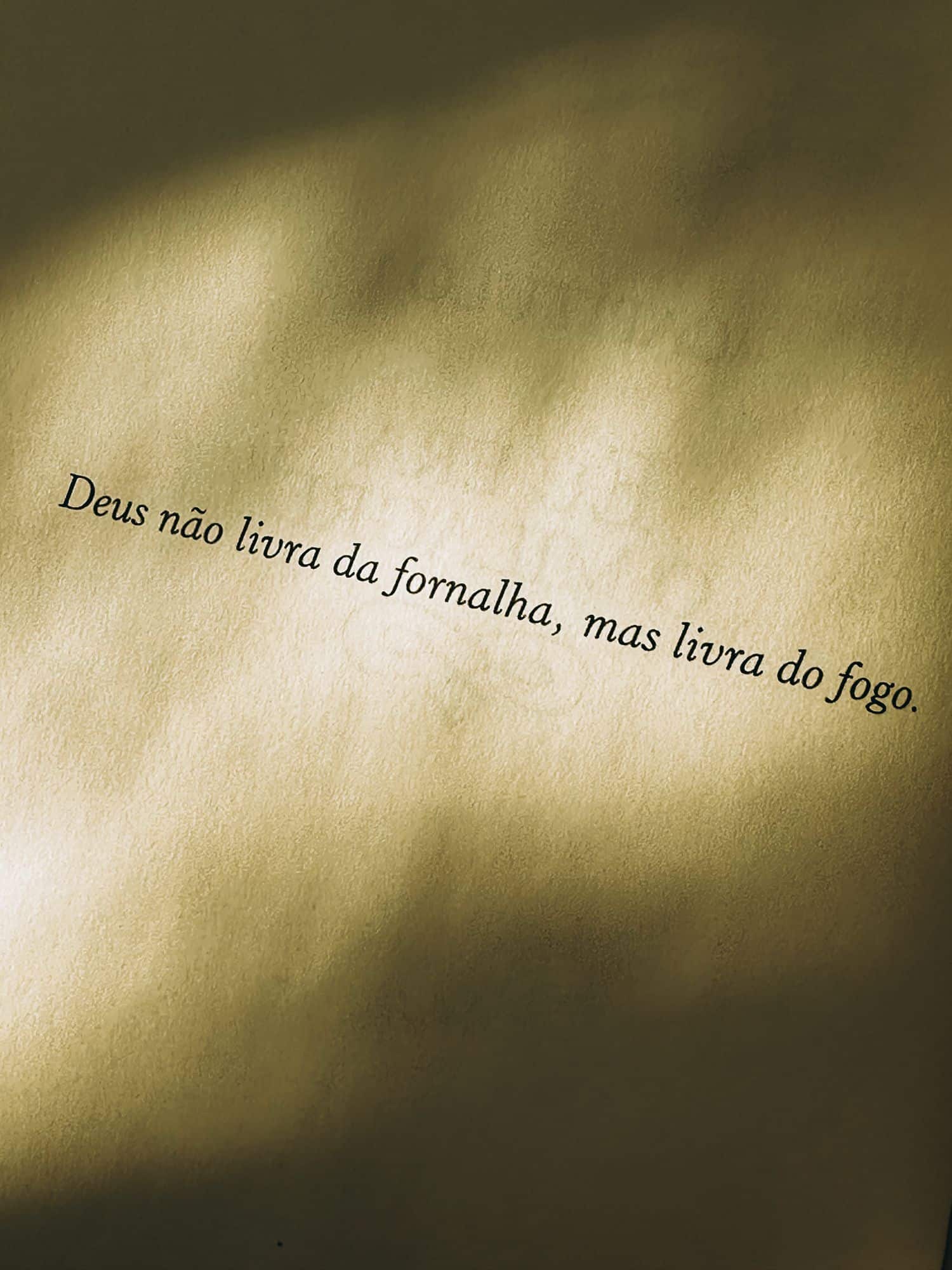 Quote 'Deus não livra da fornalha, mas livra do fogo' on textured paper with light shadows.