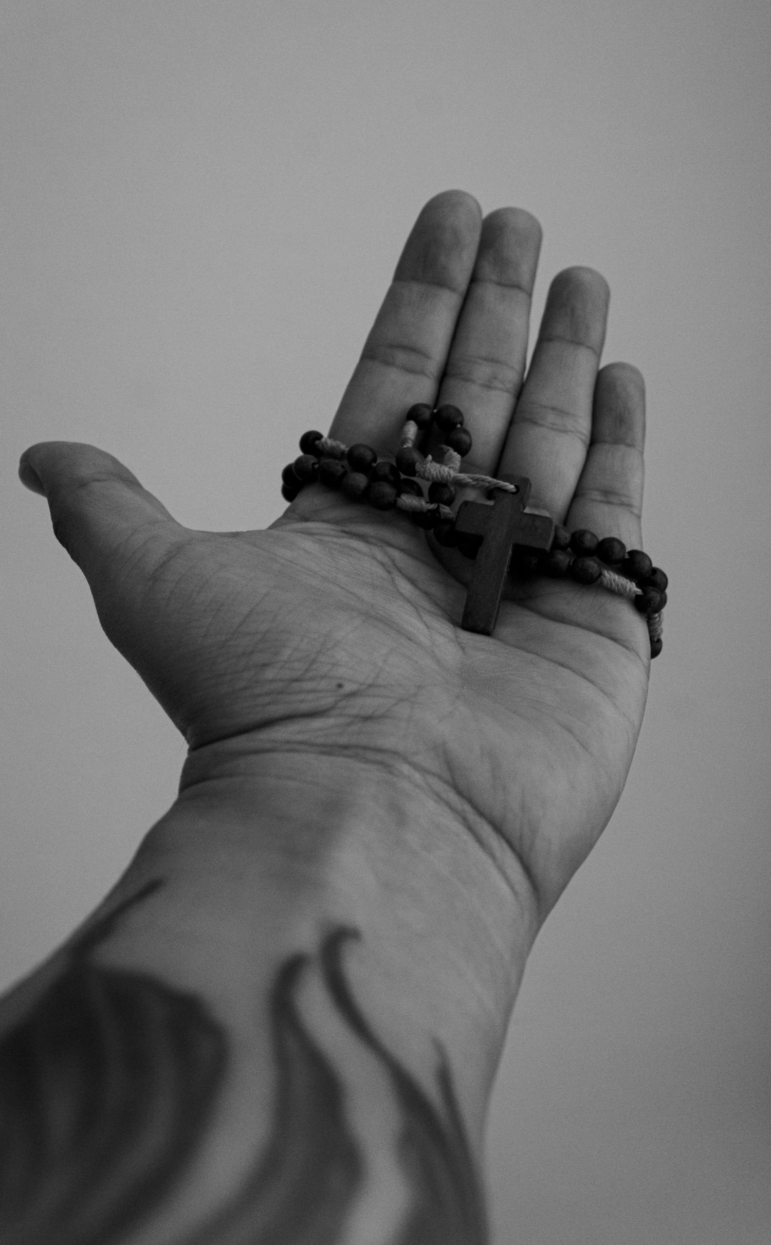 Monochrome photo of a tattooed hand holding a rosary with a cross.