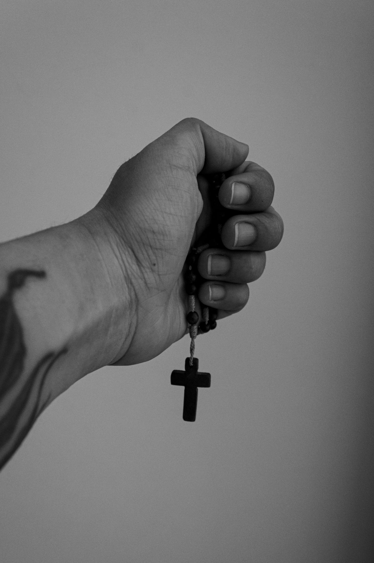 Monochrome image of a tattooed hand holding a rosary with a cross.