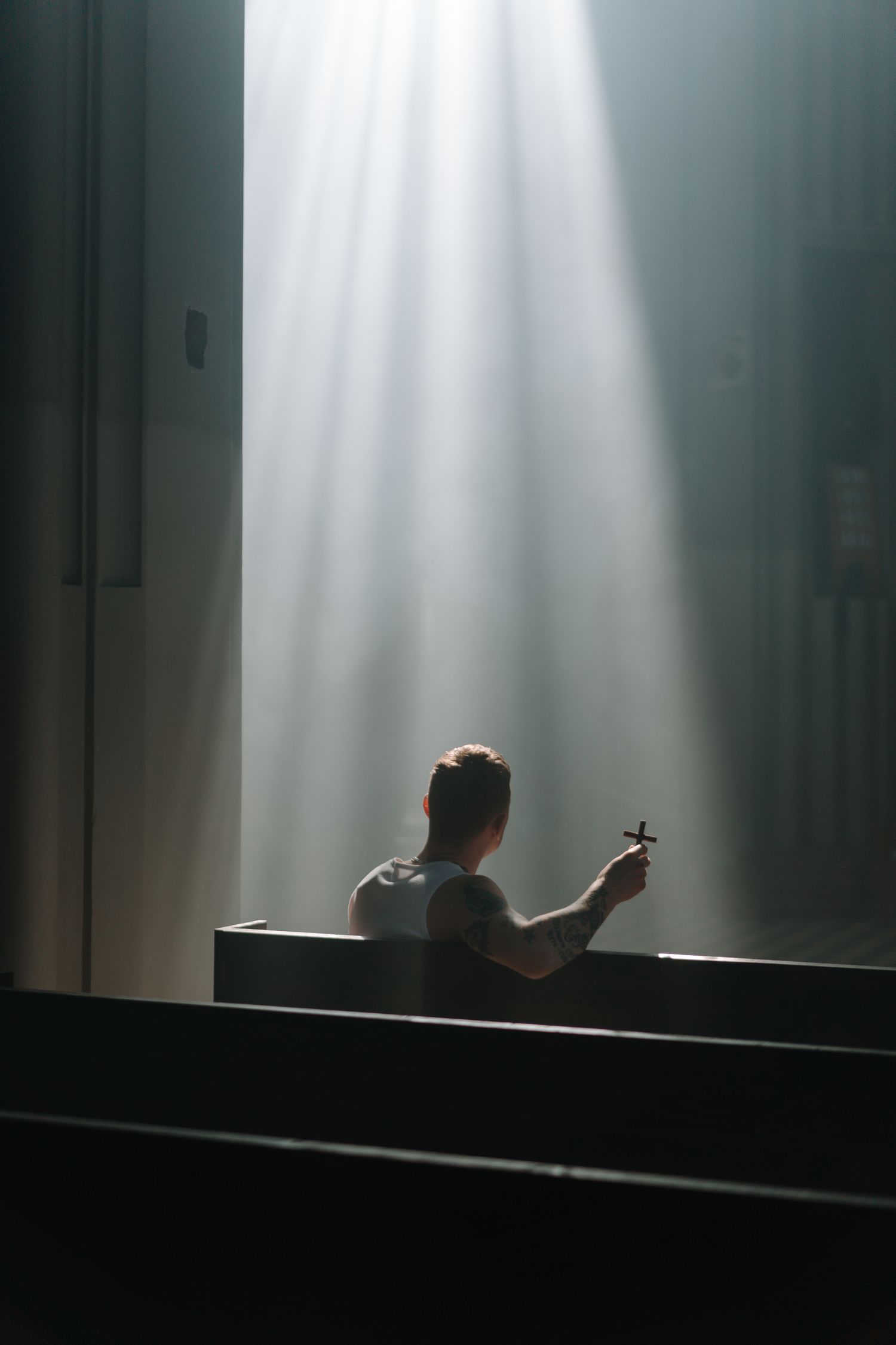 A man sits in a sunlit church pew holding a cross, reflecting spirituality and faith.