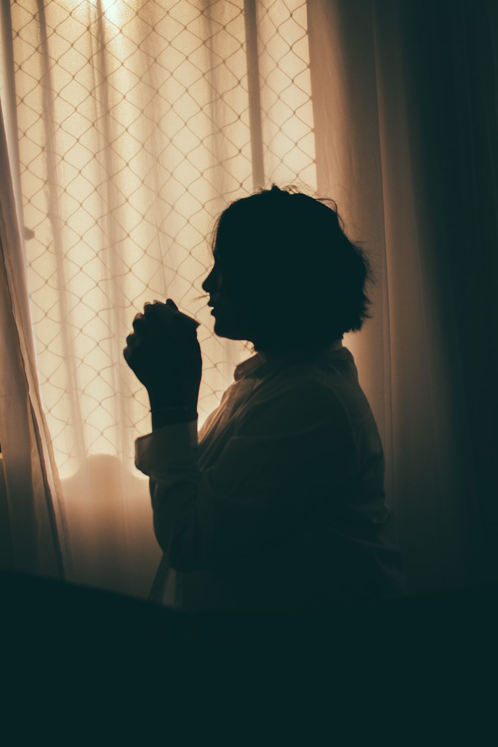 Cozy indoor scene with silhouette of a woman drinking by the window.