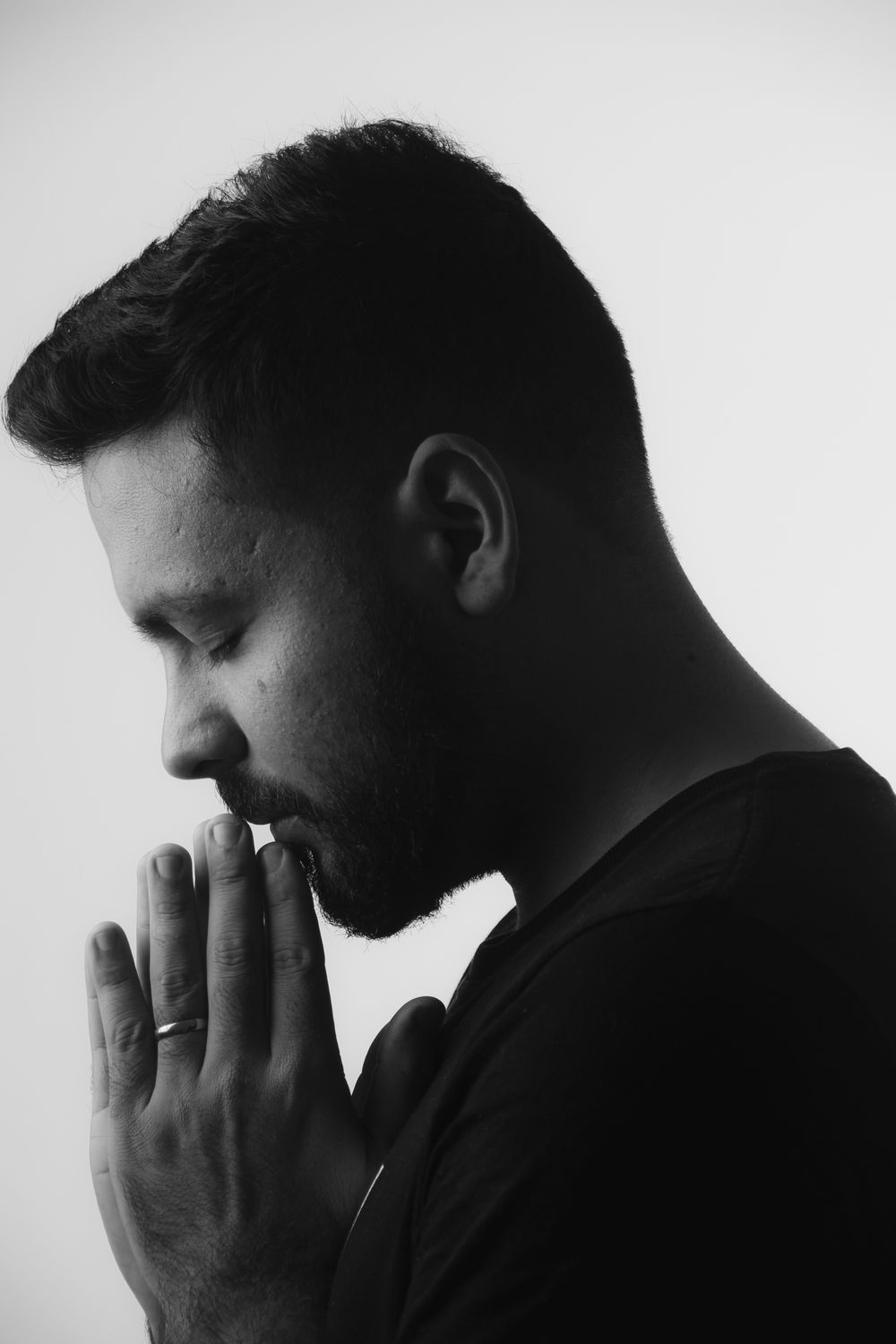 Side view monochrome portrait of a man praying with eyes closed.