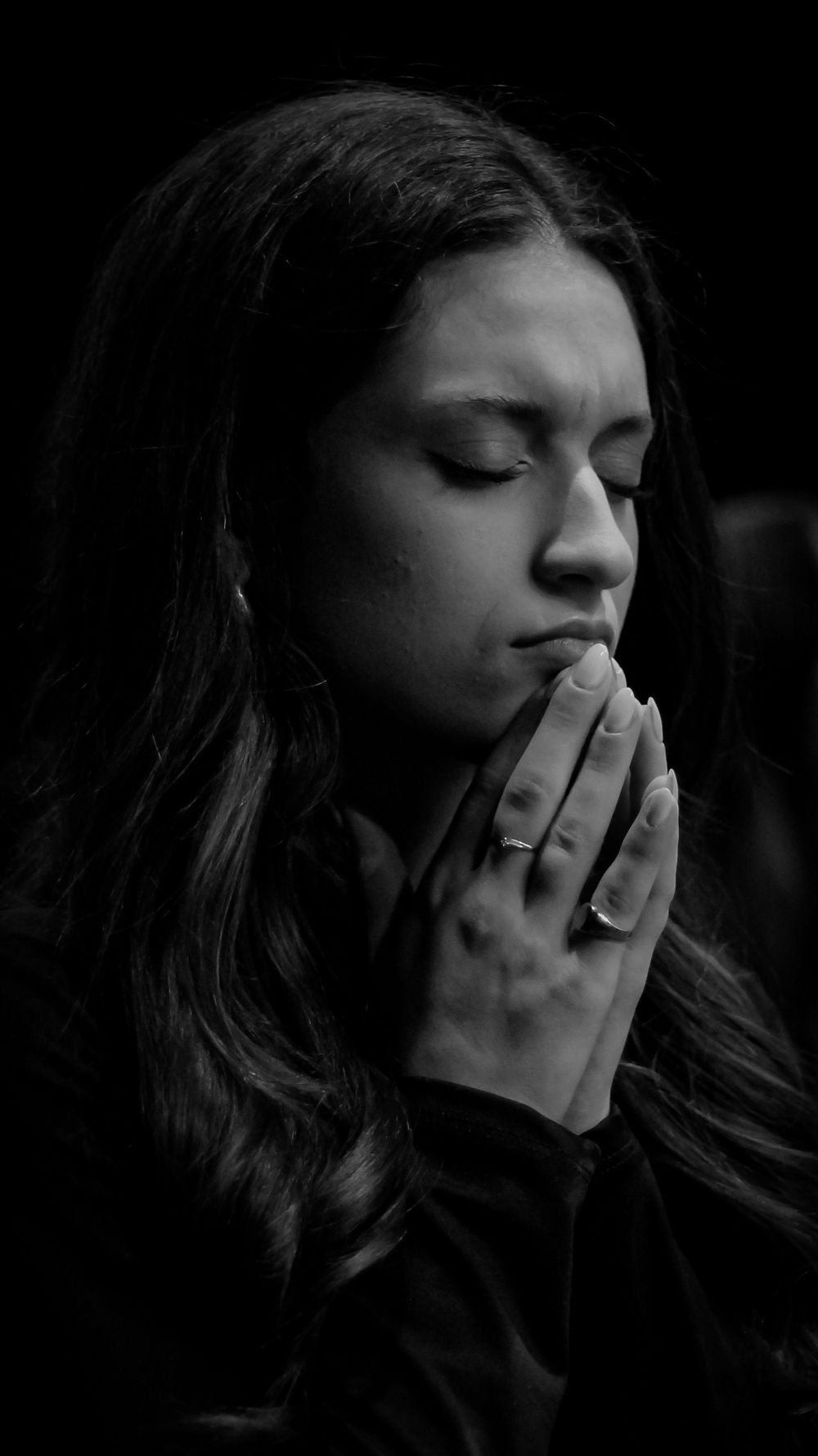 Black and white portrait of a woman with hands clasped in prayer, eyes closed.