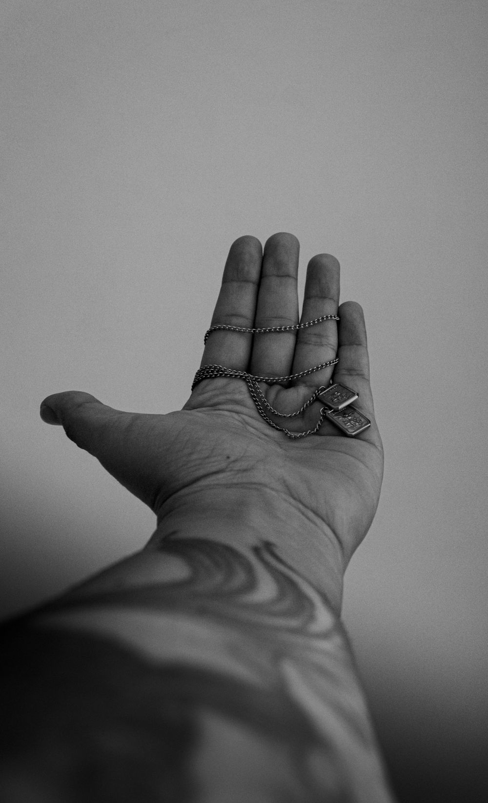 Black and white photo of a tattooed arm holding a pendant. Artistic and moody composition.