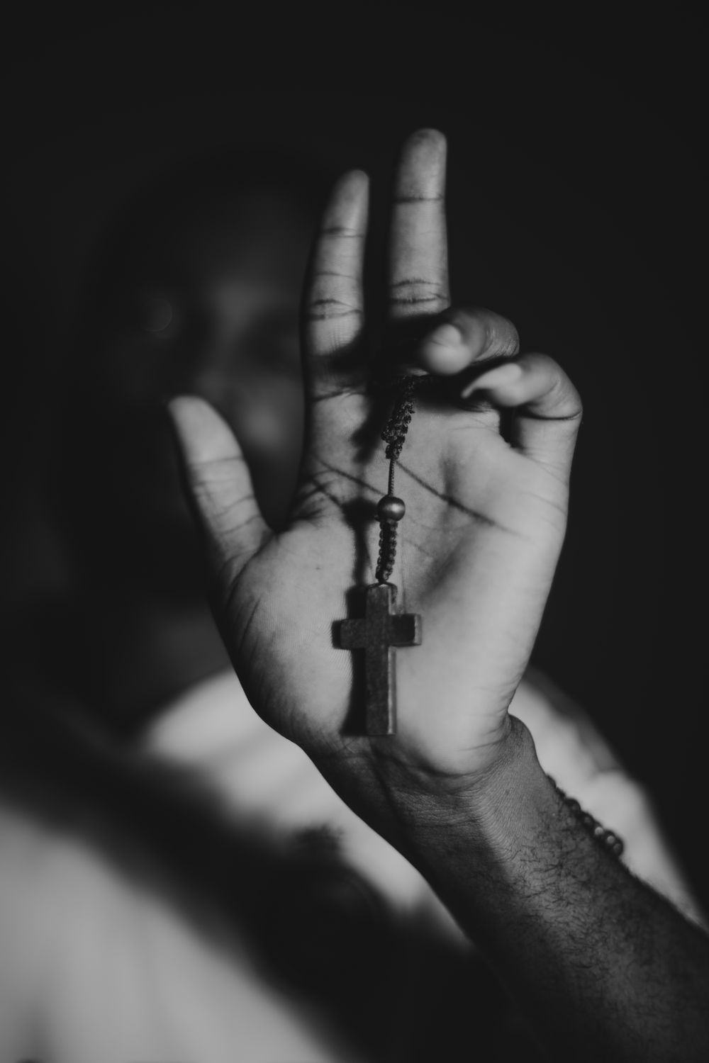 Monochrome image of an outstretched hand holding a rosary with a cross in focus, symbolizing faith and spirituality.