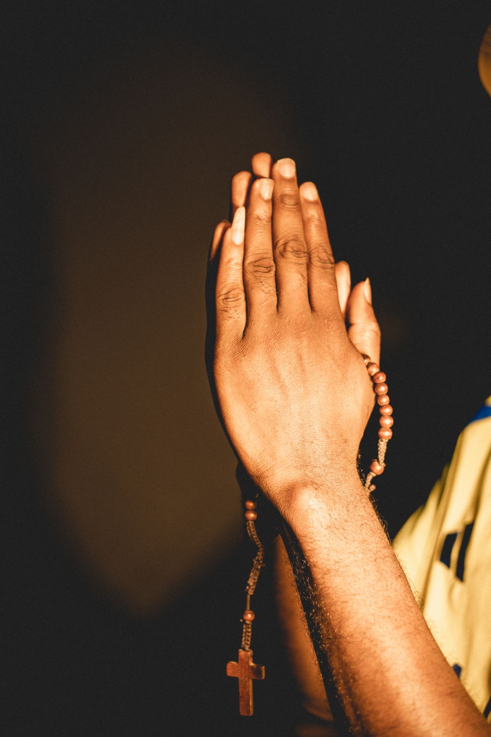 A close-up image of hands clasped in prayer holding a rosary with a cross pendant.