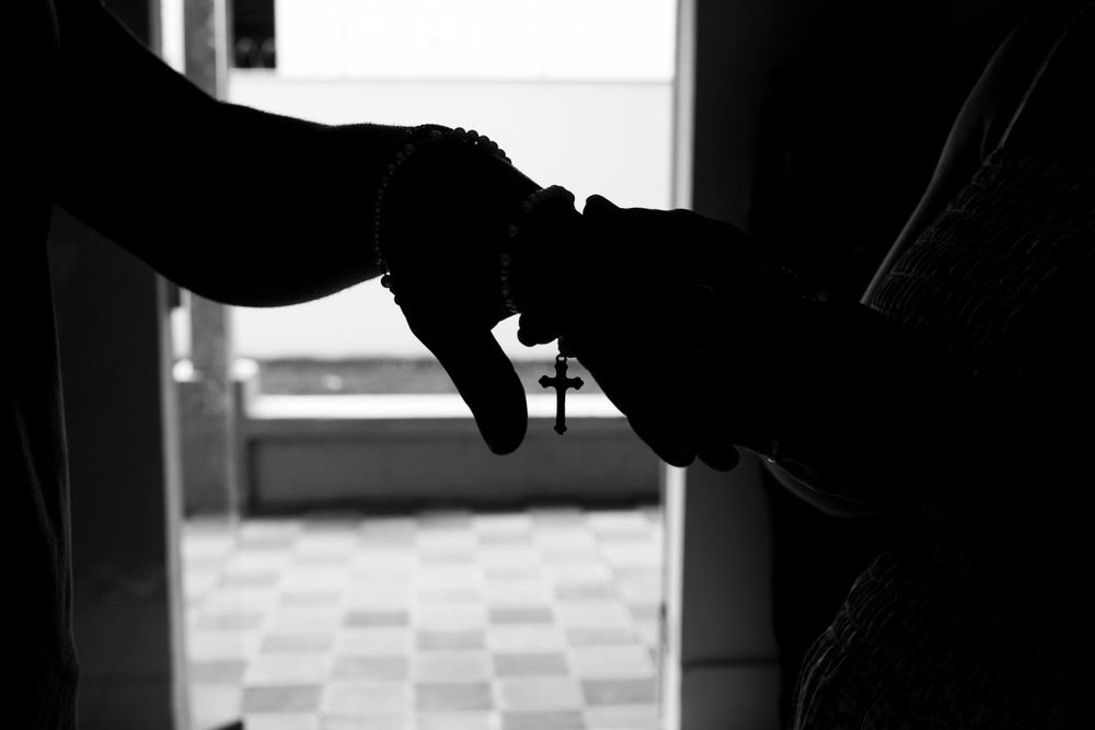 Black and white photo of hands holding a rosary with a cross, symbolizing faith and spirituality.