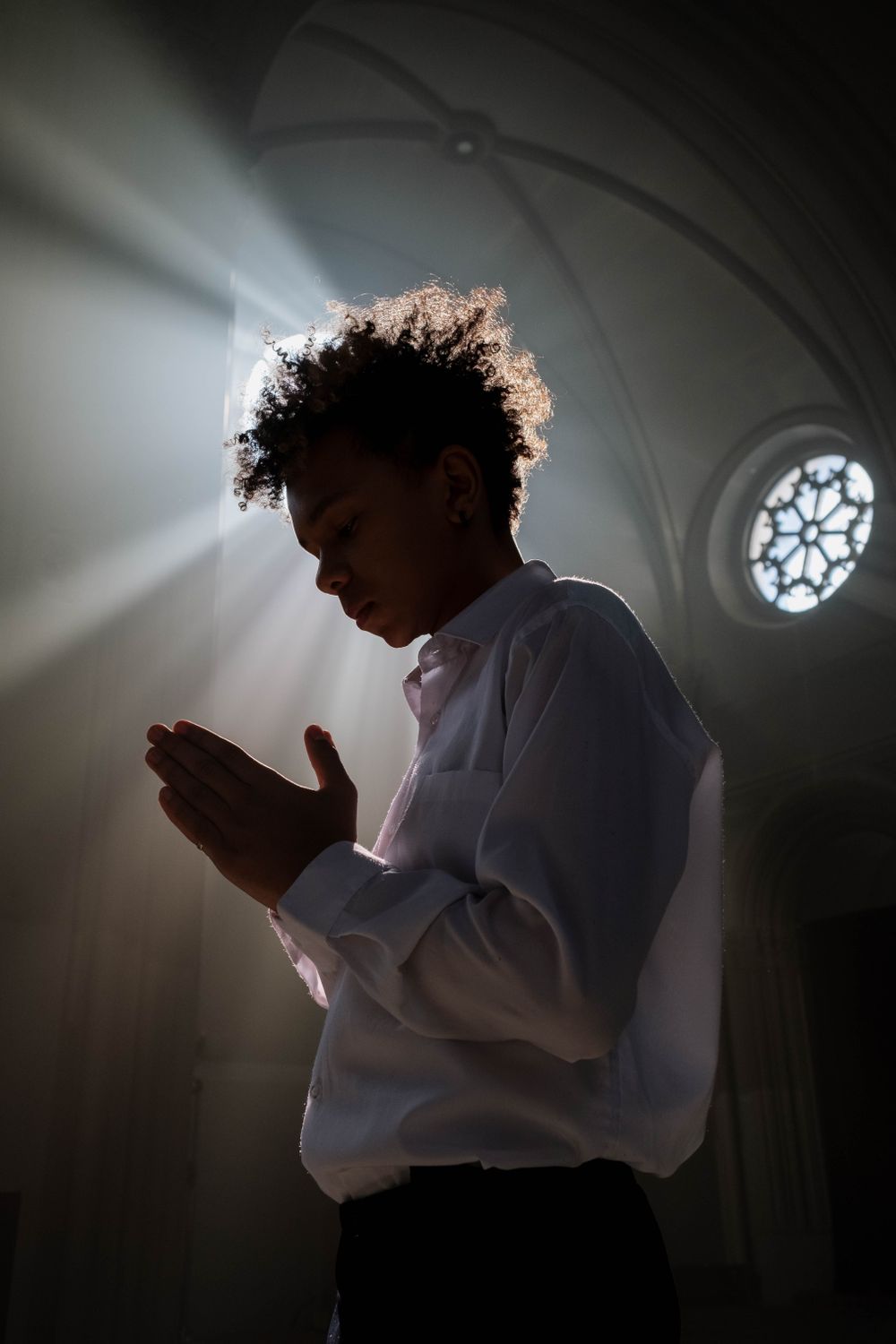 Profile of a teenager in prayer inside a sunlit church, highlighting spirituality and serenity.