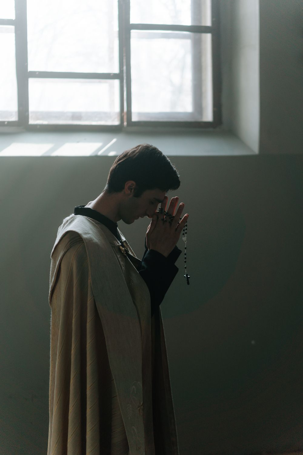 A solemn priest in vestment praying with rosary in an atmospheric church setting.